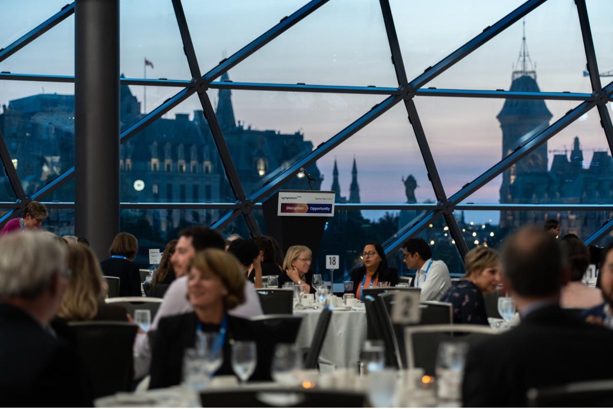 Symposium dinner attendees seated at tables with a shot of the Parliament buildings behind them.